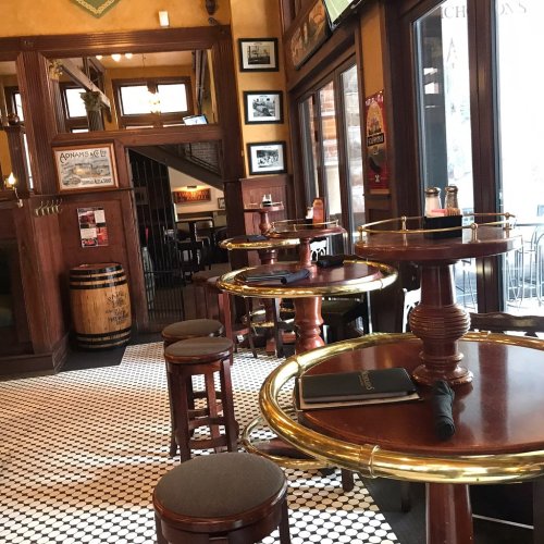 A cozy restaurant interior featuring wooden tables, stools, and a tiled floor, with warm lighting and vintage decor.