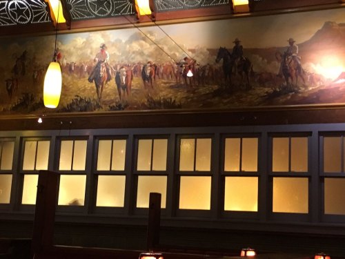 A mural depicting cowboys on horseback in a rustic setting, illuminated by warm lighting in a cozy restaurant.