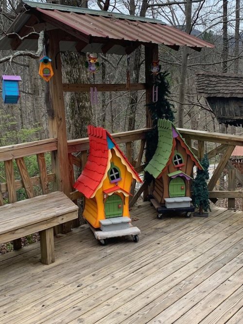 Colorful miniature houses with whimsical roofs on a wooden deck surrounded by trees.