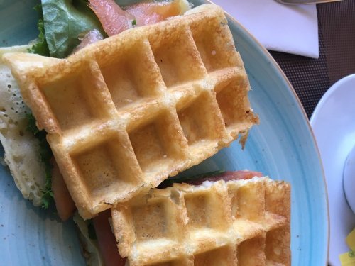 A close-up of a waffle sandwich filled with greens and salmon, served on a blue plate.