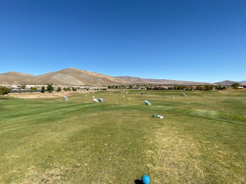 A scenic view of a golf course with rolling hills and a clear blue sky in the background.