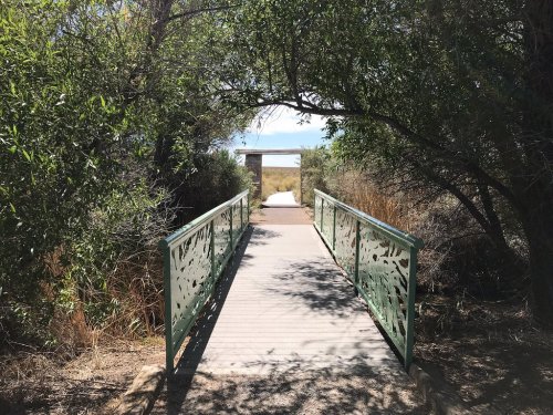 A green bridge leads through trees to a stone archway, with a path visible beyond.