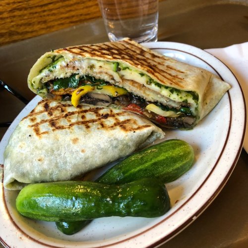 A grilled wrap filled with vegetables, served with two small pickles on a plate.