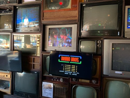 A wall of vintage TVs displaying various shows, with a central screen showing the title screen of "Mario Bros." game.