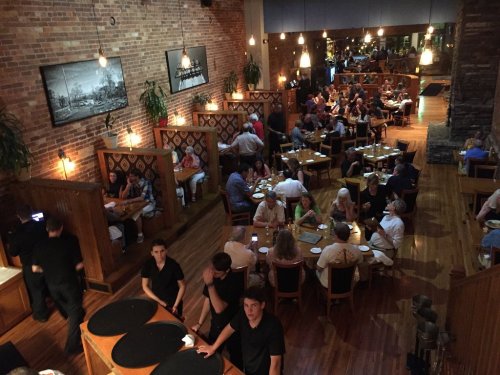 A bustling restaurant scene with diners at tables and booths, warm lighting, and staff attending to guests.