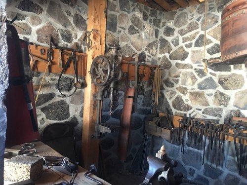 A rustic workshop with stone walls, featuring various tools, a workbench, and hanging equipment.