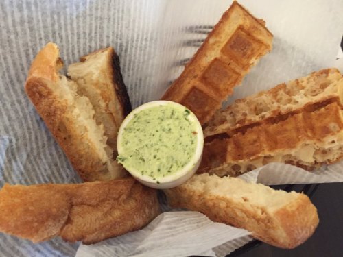 A plate with toasted bread sticks arranged around a small bowl of green herb butter.