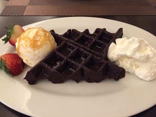 A plate with a chocolate waffle, a scoop of ice cream drizzled with caramel, whipped cream, and fresh strawberries.