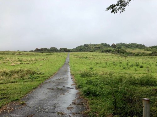 A winding path leads through a grassy landscape under a cloudy sky, with hills in the distance.
