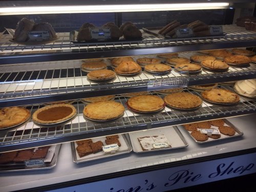 A display case filled with various pies and desserts, including fruit pies and cookies, at a pie shop.