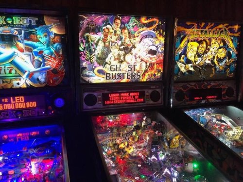A row of colorful pinball machines, featuring "Ghostbusters" prominently in the center with vibrant artwork.