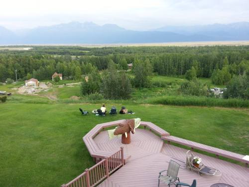 A scenic view from a deck overlooking a lush green landscape and mountains in the distance, with people relaxing below.