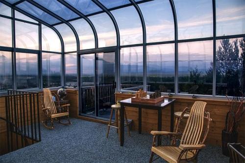 A cozy glass-enclosed room with wooden furniture, overlooking a scenic landscape at sunset.
