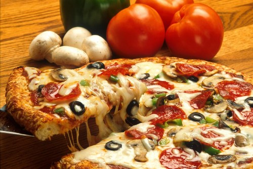 A delicious pizza topped with pepperoni, olives, mushrooms, and green peppers, with fresh tomatoes and mushrooms nearby.