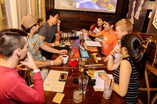 A group of friends enjoying drinks and food at a restaurant, engaged in lively conversation around a table.