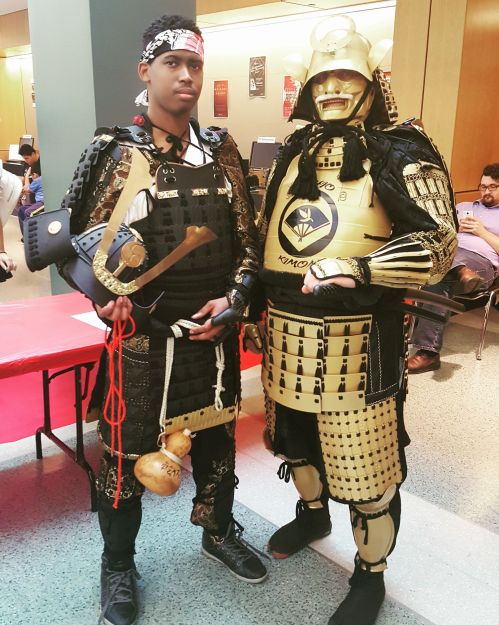 Two individuals in elaborate samurai costumes pose together, showcasing detailed armor and accessories.