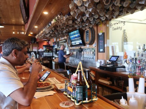 A man sits at a bar enjoying food, while a bartender serves drinks in a lively restaurant setting.