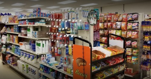 A grocery store aisle filled with snacks, toiletries, and various packaged goods on shelves and a display cart.