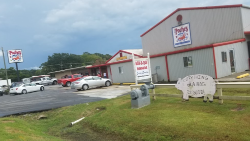 A roadside diner with a sign reading "Everything on a hog is good!" and parked cars in the lot under a cloudy sky.