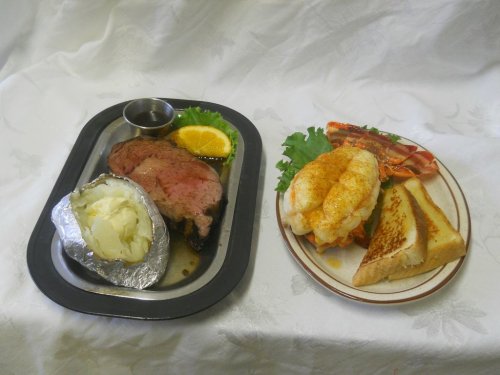 A plate with prime rib, baked potato, and a side of lobster tail with toast and garnish on a white background.