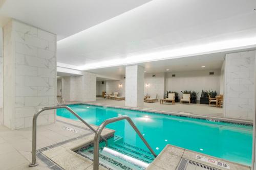 Indoor swimming pool with turquoise water, marble walls, and lounge chairs in a bright, modern space.