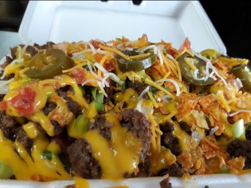 A close-up of a takeout container filled with seasoned beef, cheese, jalapeños, tomatoes, and crunchy toppings.