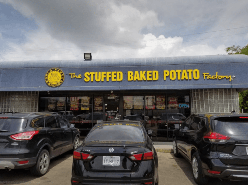 Exterior of The Stuffed Baked Potato Factory with parked cars in front and a cloudy sky above.