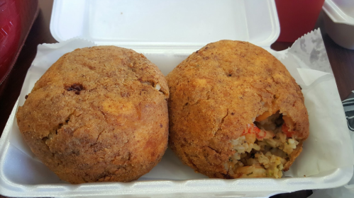 Two golden-brown, stuffed rice balls in a takeout container, with a crispy exterior and visible filling.