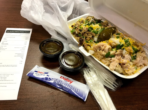 A takeout container with rice, meat, cheese, and jalapeños, accompanied by sour cream and two sauce containers.