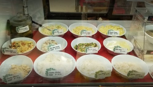A display case with various bowls of salads and dishes, each labeled with prices.