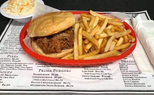 A plate with a pulled pork sandwich and a side of golden French fries, on a menu-covered table.