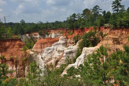 A scenic view of colorful canyon cliffs surrounded by lush greenery under a partly cloudy sky.