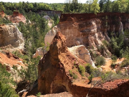 A colorful canyon with steep, layered cliffs and lush greenery in the background under a clear blue sky.