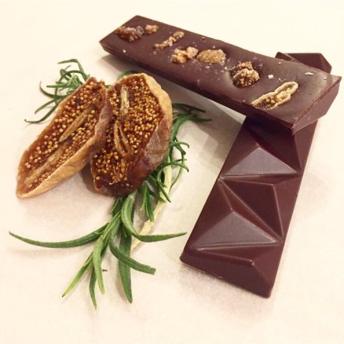 Two chocolate bars and a fig slice with seeds, arranged on a light background with fresh rosemary.