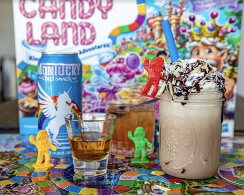 A colorful display featuring a milkshake topped with whipped cream, candy figures, drinks, and a Candy Land game backdrop.