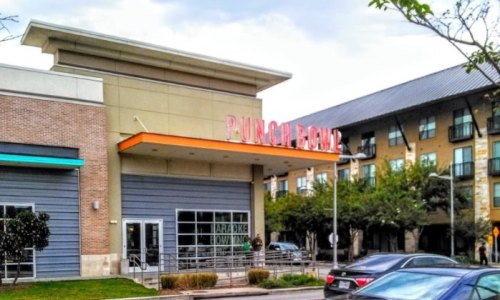 Exterior of Punch Bowl Social, a vibrant entertainment venue, with nearby apartment buildings and parked cars.