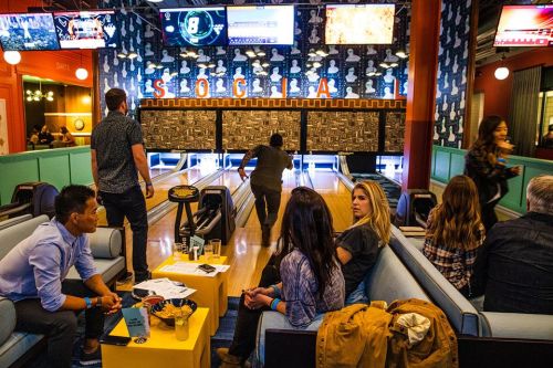 A lively bowling alley scene with people socializing, bowling, and enjoying snacks in a vibrant, colorful setting.