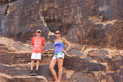 A woman and a boy pose in front of ancient petroglyphs on a rocky surface.