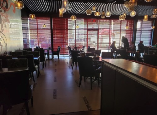 Interior of a restaurant with dark furniture, large windows, and pendant lights, featuring diners at tables.