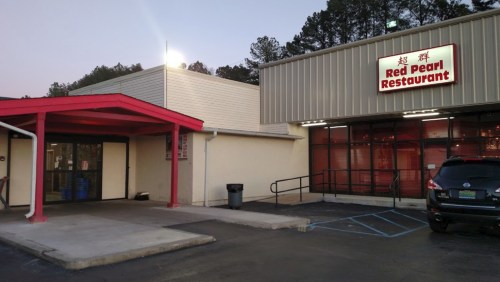 Exterior of Red Pearl Restaurant, featuring a red awning and large windows, with a parking area in front.