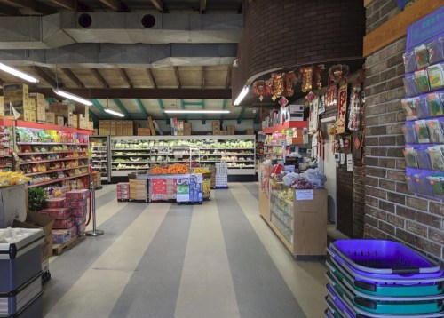 A spacious grocery store aisle filled with fresh produce, snacks, and colorful displays on shelves.