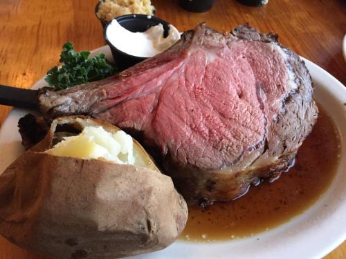 A large, juicy prime rib served with a baked potato and a side of sour cream on a white plate.