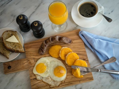 A wooden board with two fried eggs, sausage, sliced fruit, toast with butter, orange juice, and coffee.