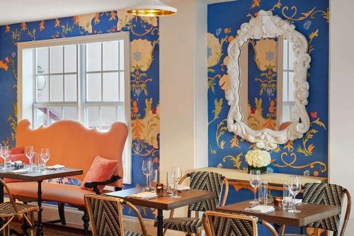 Cozy restaurant interior with floral wallpaper, a large mirror, and elegant tables set for dining.
