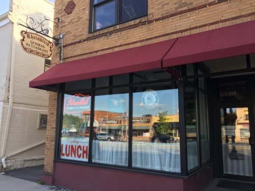 Exterior of a German restaurant with a red awning, sign, and large windows displaying a "Lunch" sign.
