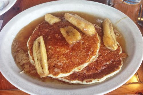 A plate of fluffy pancakes topped with caramelized bananas and drizzled with syrup.