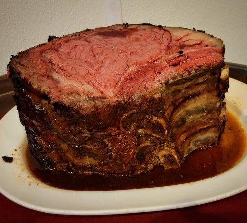 A large, juicy prime rib roast on a white platter, with a rich brown sauce and a pink, tender interior.
