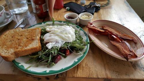 A plate with a salad, poached egg, whole grain toast, and a side of crispy bacon on a rustic wooden table.