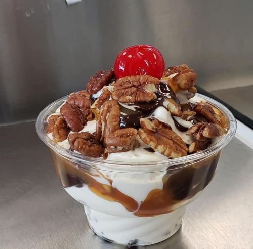 A delicious dessert cup with layers of ice cream, caramel, chocolate sauce, pecans, and topped with a cherry.
