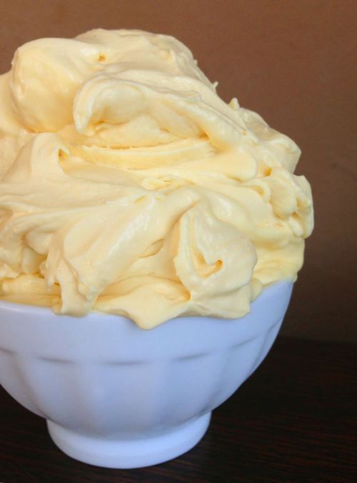 A white bowl filled with creamy, yellow butter or frosting, showcasing a smooth and fluffy texture.